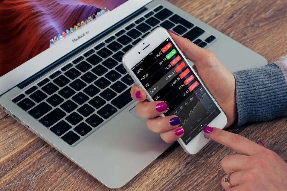 Dizüstü bilgisayar başında iPhone ekranında Apple Ads kampanya sonuçlarını kontrol eden kişi