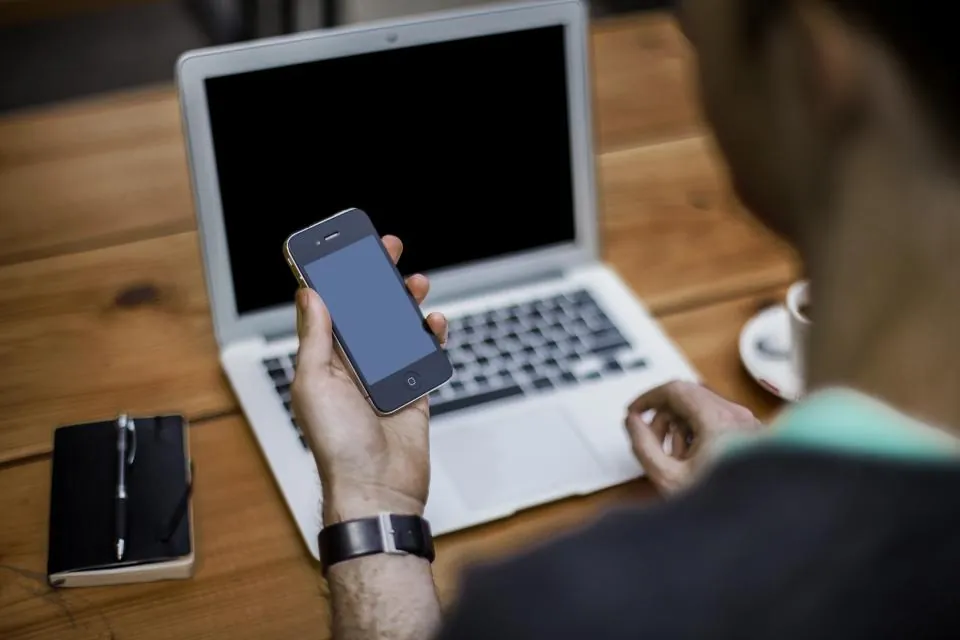 Dizüstü bilgisayar başında telefonla araştırma yapan kişi, ChatGPT ile ürün ve hizmet karşılaştırması
