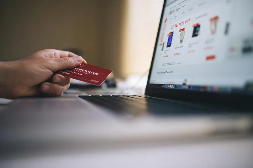 Elinde kredi kartıyla dizüstü bilgisayardan online alışveriş yapan kullanıcı