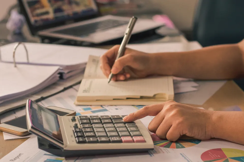 Hesap makinesi ve defterle bütçe hesaplayan kişi, kurumsal web sitesi fiyatını planlıyor